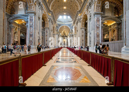 A wide angle interior view inside St Peter's Basilica with tourists walking around.