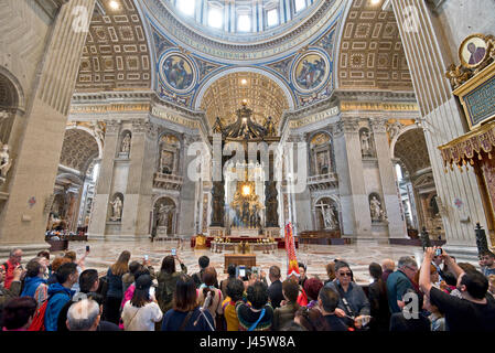 A wide angle interior view inside St Peter's Basilica of the main alter and crowds of tourists and visitors all trying to get photographs and selfies. Stock Photo