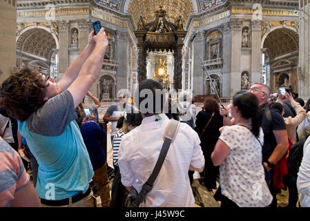 A wide angle interior view inside St Peter's Basilica of the main alter and crowds of tourists and visitors all trying to get photographs and selfies.