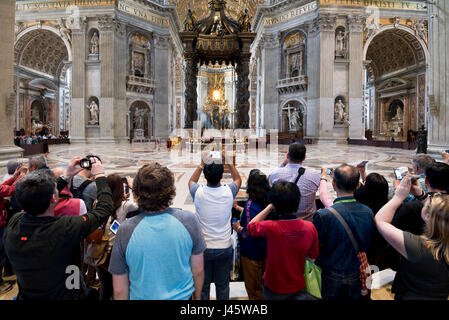 A wide angle interior view inside St Peter's Basilica of the main alter and crowds of tourists and visitors all trying to get photographs and selfies. Stock Photo