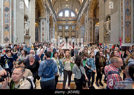 A wide angle interior view inside St Peter's Basilica of the main alter and crowds of tourists and visitors. Stock Photo