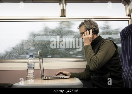 Train UK. Mature man with laptop at window seat on empty train with rain on window. England. United Kingdom Stock Photo