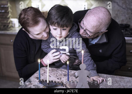 Jewish Family of grandparents and grandson lighting Hanukkah Candles in a menorah for the holdiays Stock Photo