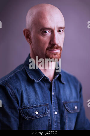 Portrait of a sad and angry looking bald man with a red goatee wearing a blue denim chambray cowboy shirt Stock Photo