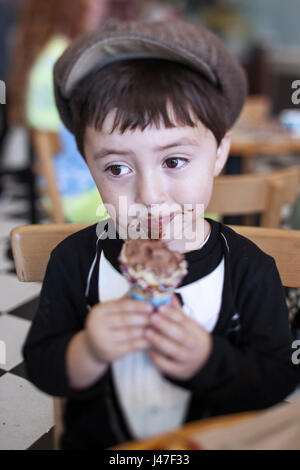 Cute little boy in a brown newsboy cap and tuxedo t-shirt eating a messy chocolate ice cream cone Stock Photo