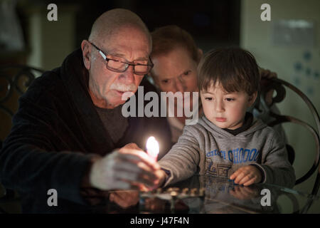 Jewish family of grandparents and their grandson lighting Hanukkah Candles in a menorah for the holdiays Stock Photo