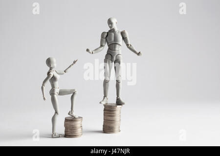 Income inequality concept shown with realistic male and female figurines standing on piles of coins. Female figurine extending hand towards male Stock Photo