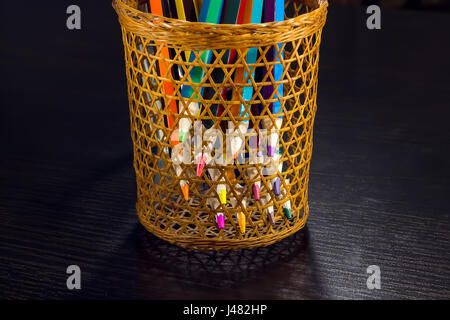 Sharp tips of colored pencils sharpen from sections of a wicker tube, on a dark wooden background Stock Photo