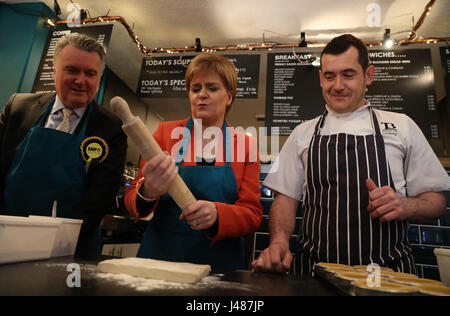 SNP Leader Nicola Sturgeon holds a rolling pin as she and the party's local candidate John Nicolson (left) make haggis pies with Table 13 Express co-owner Iain Murphy on a campaign visit to the cafe in Kirkintilloch, East Dunbartonshire. Stock Photo