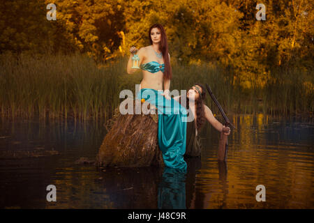 Fairytale sad woman sitting on a stump in the marshes, in the back looks fabulous man. Stock Photo