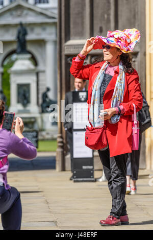 A female chinese tourist, with a red coat and bag and a flowery hat, poses for a photograph in front of the main entrance to King's college at the uni Stock Photo