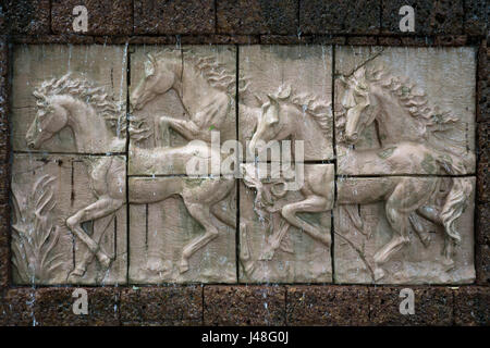 Stone sculpture of horses on wall with waterfall Stock Photo