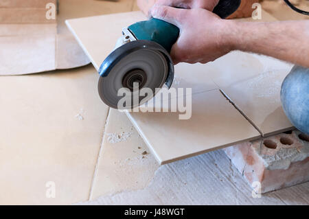 A construction worker cutting a tile using an angle grinder Stock Photo