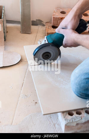 A construction worker cutting a tile using an angle grinder Stock Photo