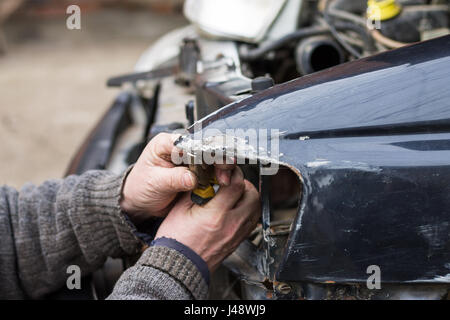 Repair service worker fix damaged car after crash on the road. Working with pliers to align metal body. Stock Photo