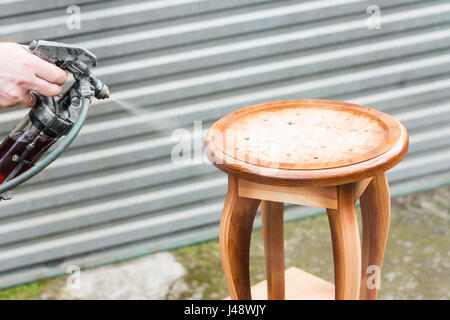 Side view of serious middle aged carpenter using spray gun for painting  wood detail with white