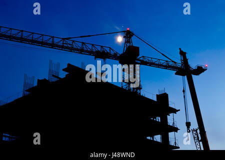 Construction Site. Industrial construction cranes and building silhouettes on night sky. Beautiful colorful night landscape. Stock Photo