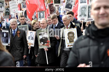 Russian President Vladimir Putin, center, holds a portrait of his war veteran father Vladimir Spiridonovich Putin, as he marches alongside former Soviet artist Vasily Lanovoya during the Immortal Regiment patriotic march marking the annual Victory Day celebrations and the 72nd anniversary of the end of World War II in Red Square May 9, 2017 in Moscow, Russia. Stock Photo