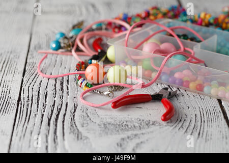 Box with beads, plier and glass hearts to create hand made jewelry on old wooden background. Handmade accessories Stock Photo