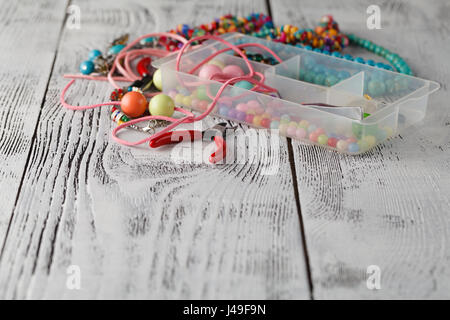 Box with beads, plier and glass hearts to create hand made jewelry on old wooden background. Handmade accessories Stock Photo