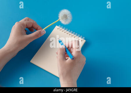 Human hands with pencil writing on paper and hold dandelion Stock Photo