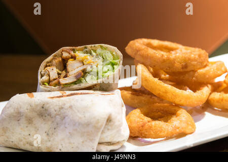 A chicken caesar wrap, served with large onion rings on a white plate. Stock Photo