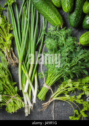 Fresh green vegetables and herbs spread out on a black stone background. Stock Photo