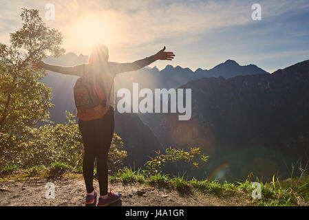 Woman traveller meet new day on sunrise mountain landscape. Excited woman stand with hands up Stock Photo