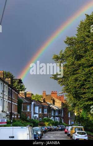 A bright rainbow on a rainy summer afternoon over a residential street of Victorian terraced houses in Islington, North London, UK Stock Photo