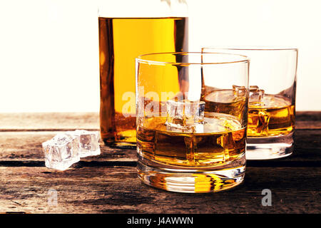 whiskey glasses and bottle on wooden table against white background Stock Photo