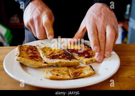 Close up view of man cutting a slice of toast on a white plate Stock Photo