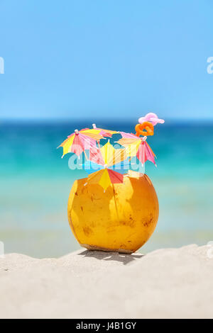 Coconut with straws and colorful cocktail umbrellas on a tropical beach, summer holiday concept, selective focus. Stock Photo