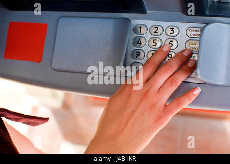 Close up of hand entering pin at an ATM. Finger about to press a pin code on a pad. Security code on an Automated Teller Machine. Female arms, ATM - e Stock Photo