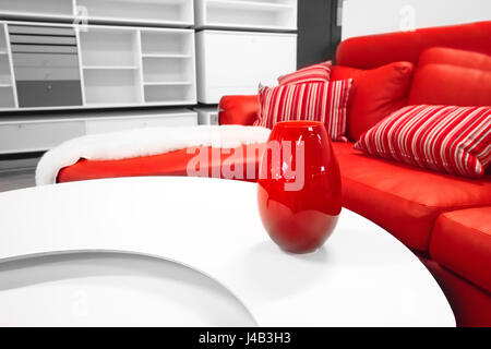 Red vase on a table in a stylish living room with a red couch with decorative pillows in white colors Stock Photo