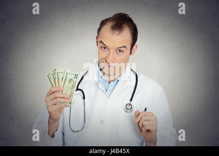 Closeup portrait grumpy greedy miserly health care professional, male doctor holding, protecting his money dollars in hand isolated grey wall backgrou Stock Photo