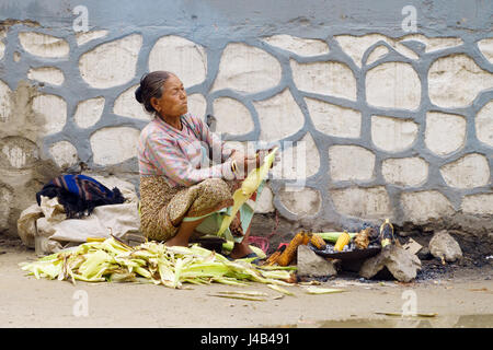 Old indigent woman roasting corn on the side of the street in heavily polluted air. Kathmandu, Nepal. Stock Photo