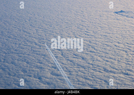 MUNICH, GERMANY - JAN 21st, 2017: airplane flies in white clouds in a blue sky and leaving trail, as seen from an other plane Stock Photo