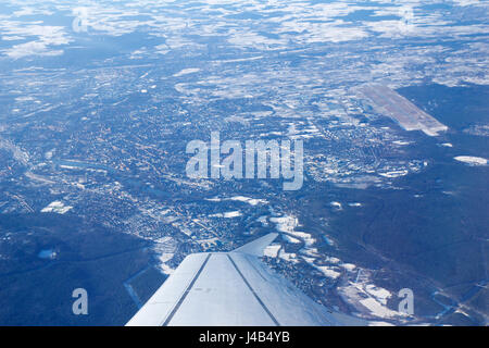 NUREMBERG, GERMANY - JAN 20th, 2017: View through aircraft window onto jet wing, wingview over snow covered city of Nuremberg in Bavaria, airport in the background Stock Photo