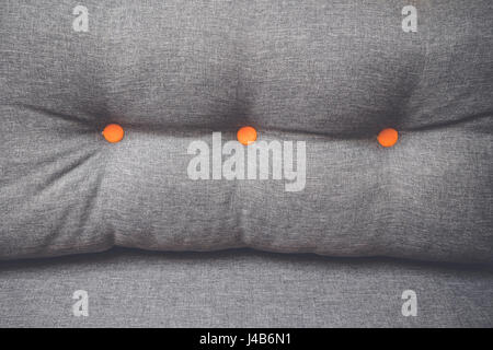 Pillow in grey color with two round orange buttons in a couch and in close-up Stock Photo