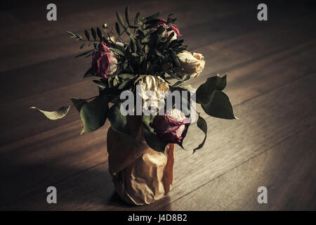 Bouquet of dried red and white roses stands on wooden table, closeup low key photo with soft selective focus, retro stylized tonal correction effect Stock Photo