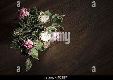 Bouquet of dried red and white roses stands on wooden table, closeup low key photo with soft selective focus. Top view Stock Photo