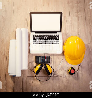 Top view of a architectonic workspace with laptop and yellow helmet. Different accessories, plans and cup of coffee is on the table. Stock Photo