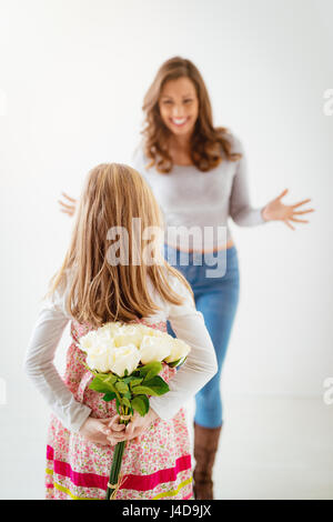 Cute daughter giving her mother bouquet white roses for Mother's Day. Selective focus. Focus on foreground, on little girl and flowers. Stock Photo