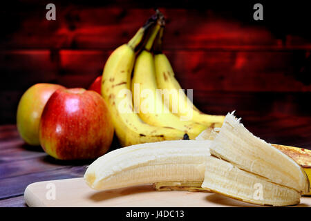 Bananas and ripe apples whole and sliced on a table in aged wood. Stock Photo