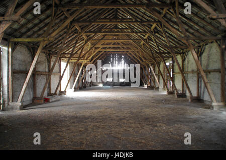 Empty rural barn with wooden supports and remains of hay on the floor Stock Photo