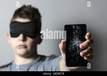 sad teen with sleep mask is worried because of breakage glass of smart phone in front of grey background Stock Photo