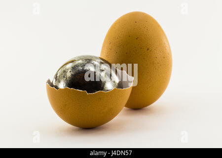 Rusty steel ball inside the shell of chicken egg and one whole chicken egg isolated on white background Stock Photo