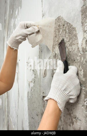 hands removing old wallpaper from wall with spatula Stock Photo