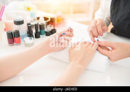 close up young woman with coloring drawing for her beautiful nail by professional manicure using nail polish brush in real salon store background. bea Stock Photo