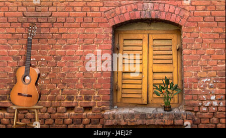 Musical background content with acoustic guitar against a red brick wall with a vintage window. Stock Photo